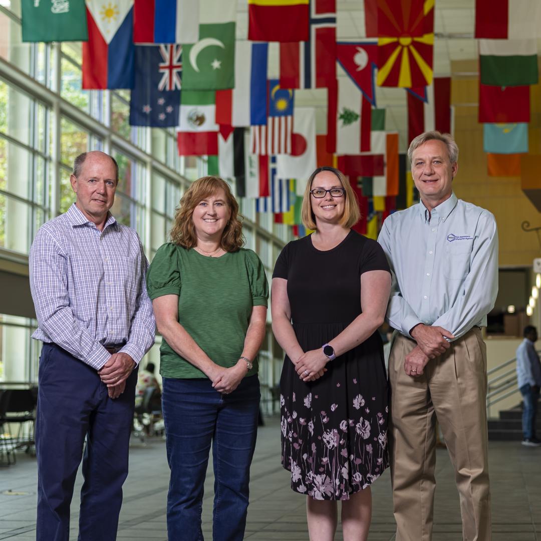  A group of ORNL staff standing in a long corridor with flags hanging from the ceiling