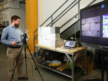 Buildings technologies researcher Philip Boudreaux uses a camera and a technique known as background-oriented schlieren photography to identify air leak sources in a concrete block wall mock-up. Credit: ORNL, U.S. Dept. of Energy