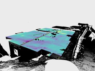 A color-enhanced 3D laser scan of a large concrete slab in a housing development, showing surface variations in shades of blue, green, yellow, and purple. Surrounding structures and terrain are rendered in black and white. The image was captured using the FLAT tool’s 360-degree scanning technology.