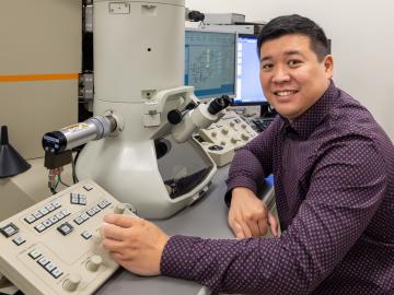 ORNL researcher is sitting at a transmission electron microscopy board in a lab at ORNL