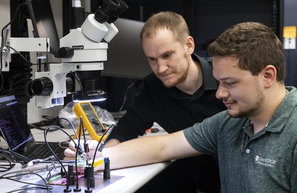 Two researchers, Logan Sturm and John Benson, work on microelectronics in ORNL's Embedded Systems Security Lab