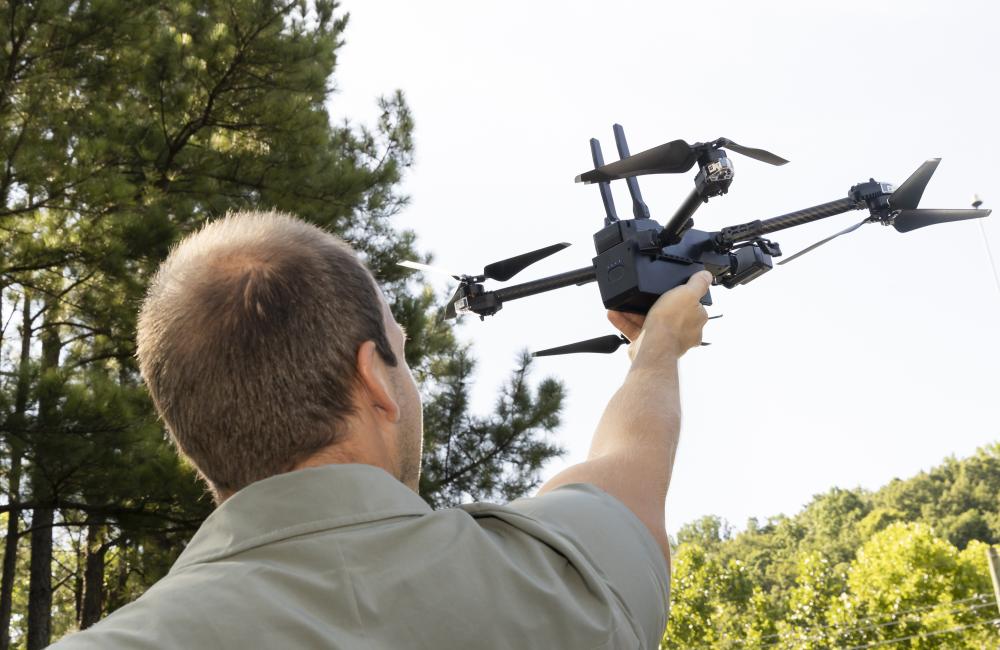 A man is photographed from behind launching a quadcopter drone from the palm of an extended arm.