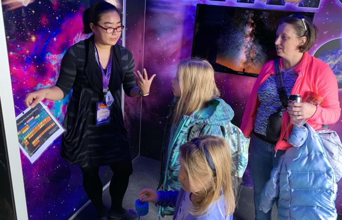 ORNL researcher Chengyun Hua explains chemical elements to Leah Pitts, 9, and her sister Madeline, 6, as their mother, Shayne looks on. The Pittses are part of Pack 50 in the Karns area of Knoxville.