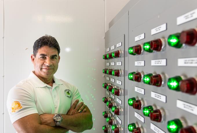 A man stands with arms crossed next to an energy system control panel