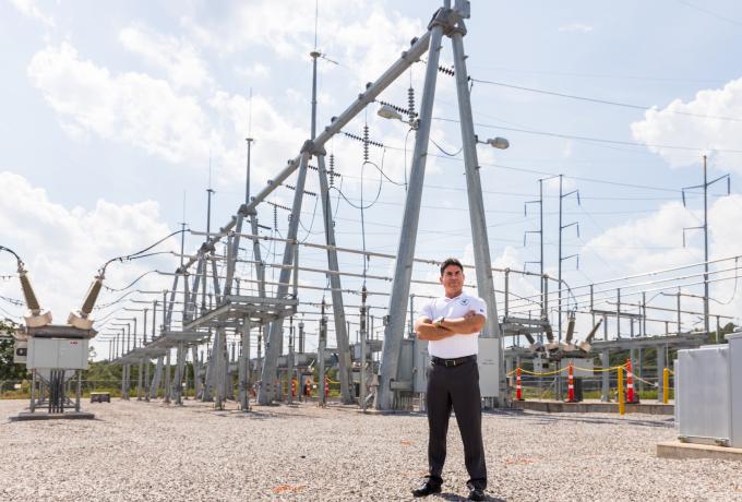A man stands in front of energy grid substation