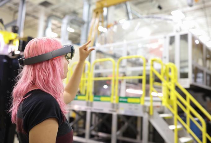artificial intelligence for manufacturing, woman with pink hair standing in manufacturing high bay with VR glasses on.