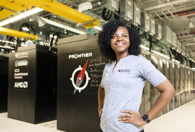 Woman with hands on hips in front of the Frontier supercomputer. 