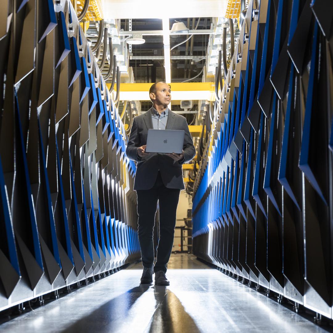 Man walking with laptop between two rows of supercomputers