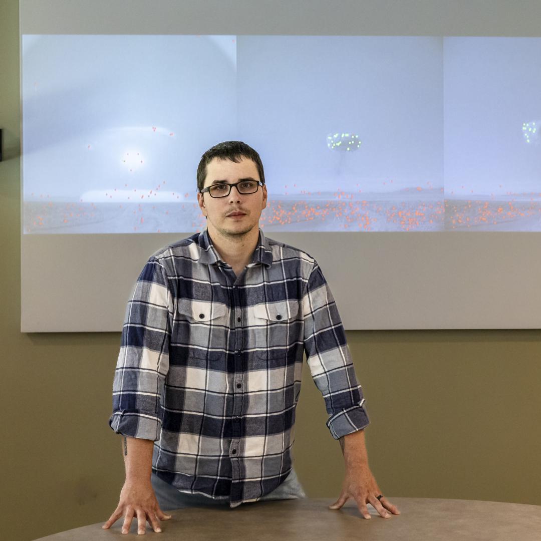 Cody Lloyd stands in front of images of historical nuclear field testing. The green and red dots are the machine learning algorithm recognizing features in the image. Credit: Carlos Jones/ORNL, U.S. Dept. of Energy
