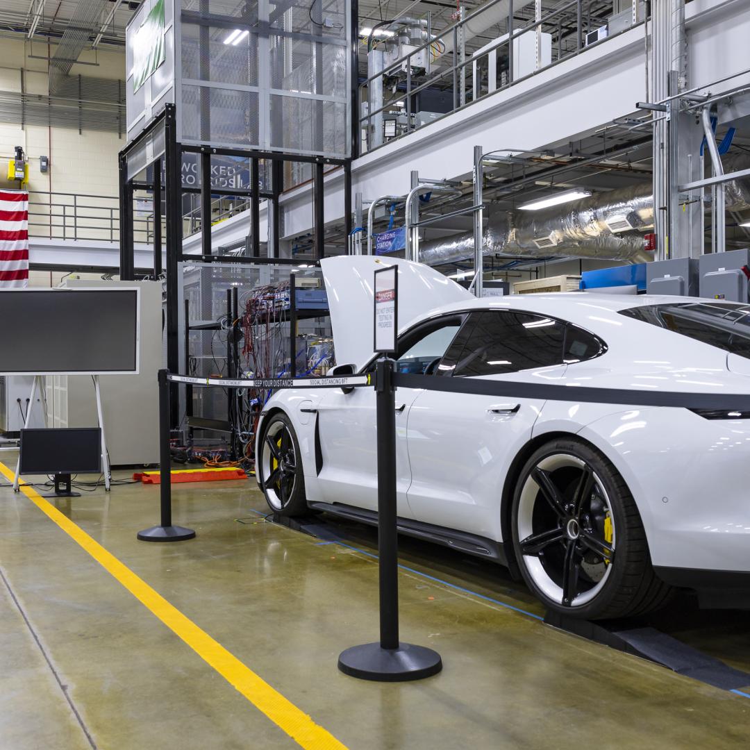 White car (Porsche Taycan) with the hood popped is inside the building with an american flag on the wall. 