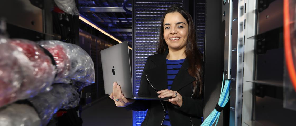 Veronica Melesse Vergara holding a laptop by the Summit supercomputer. 