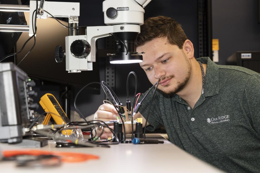 A man looks at a circuit board under a microscope.