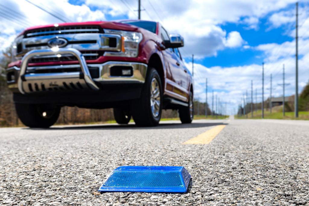Close up of a reflective road marker as a pickup truck drives past