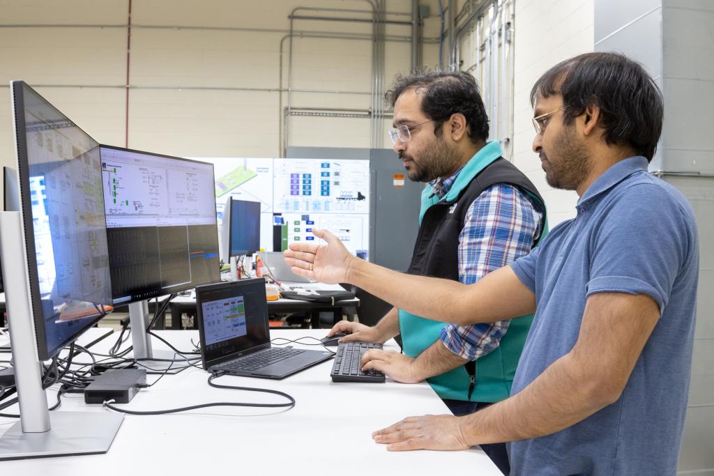 Two men gesturing at data on screens in a lab
