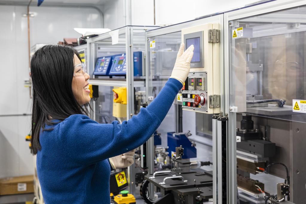 Battery researcher in a blue lab coat working in the battery manufacturing facility