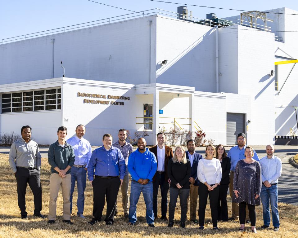 The promethium research team, standing in front of ORNL’s Radiochemical Engineering Development Center, included, from left, Santanu Roy, Thomas Dyke, Ilja Popovs, Richard Mayes, Darren Driscoll, Frankie White, Alex Ivanov, April Miller, Subhamay Pramanik, Santa Jansone-Popova, Sandra Davern, Matt Silveira, Shelley VanCleve and Jeffrey Einkauf. Credit: Carlos Jones/ORNL, U.S. Dept. of Energy