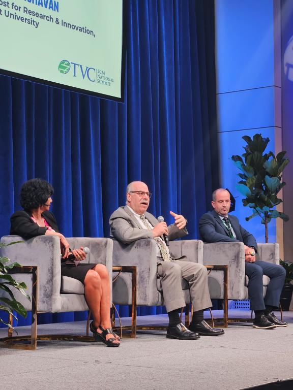 People sitting in chairs on a stage presenting during a panel discussion