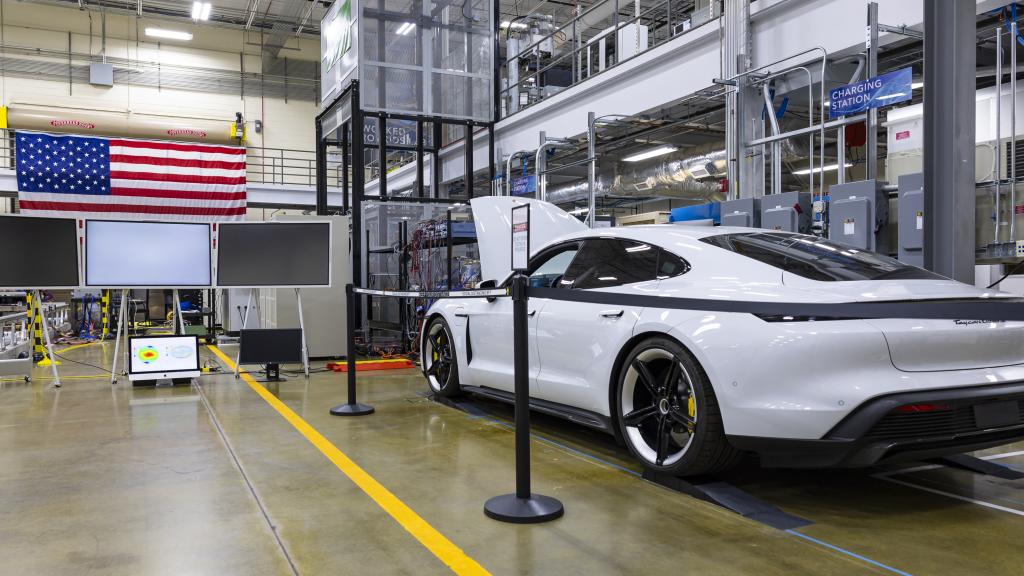 White car (Porsche Taycan) with the hood popped is inside the building with an american flag on the wall. 