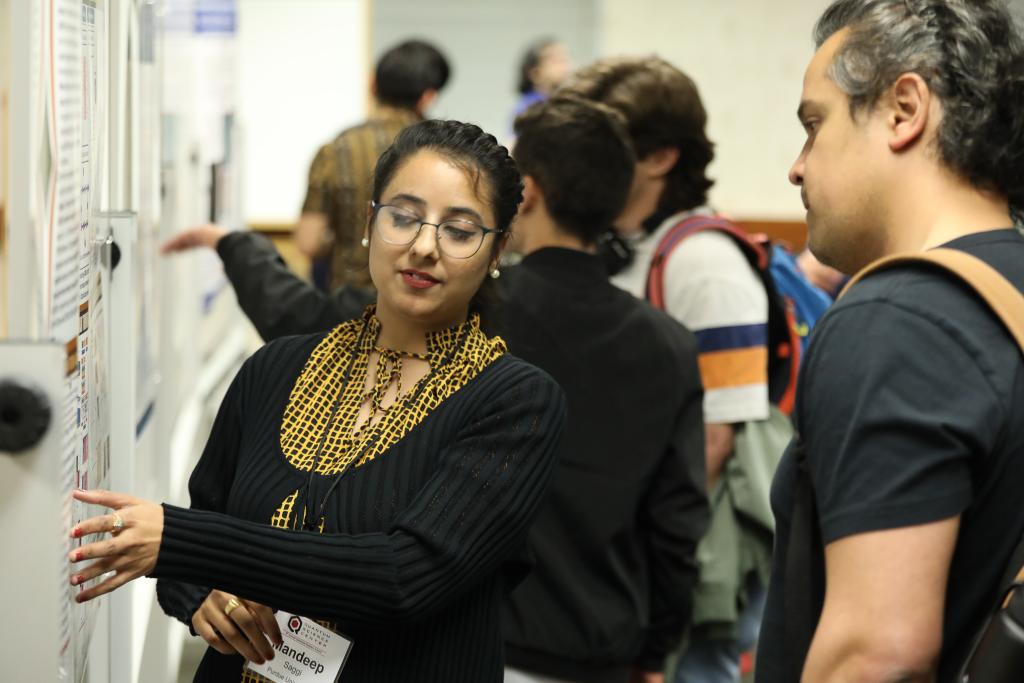 Woman explaining her poster session, pointing to it. 