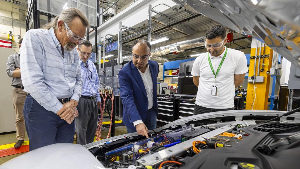 researchers gathered around car engine discussing EV battery