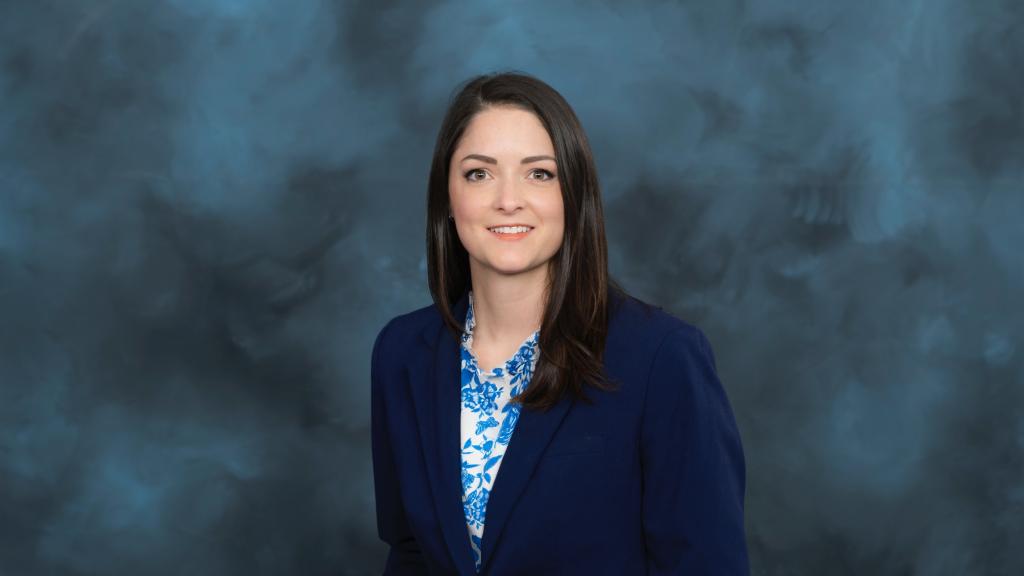 woman in a blue blazer and blue and white shirt smiles for a photo