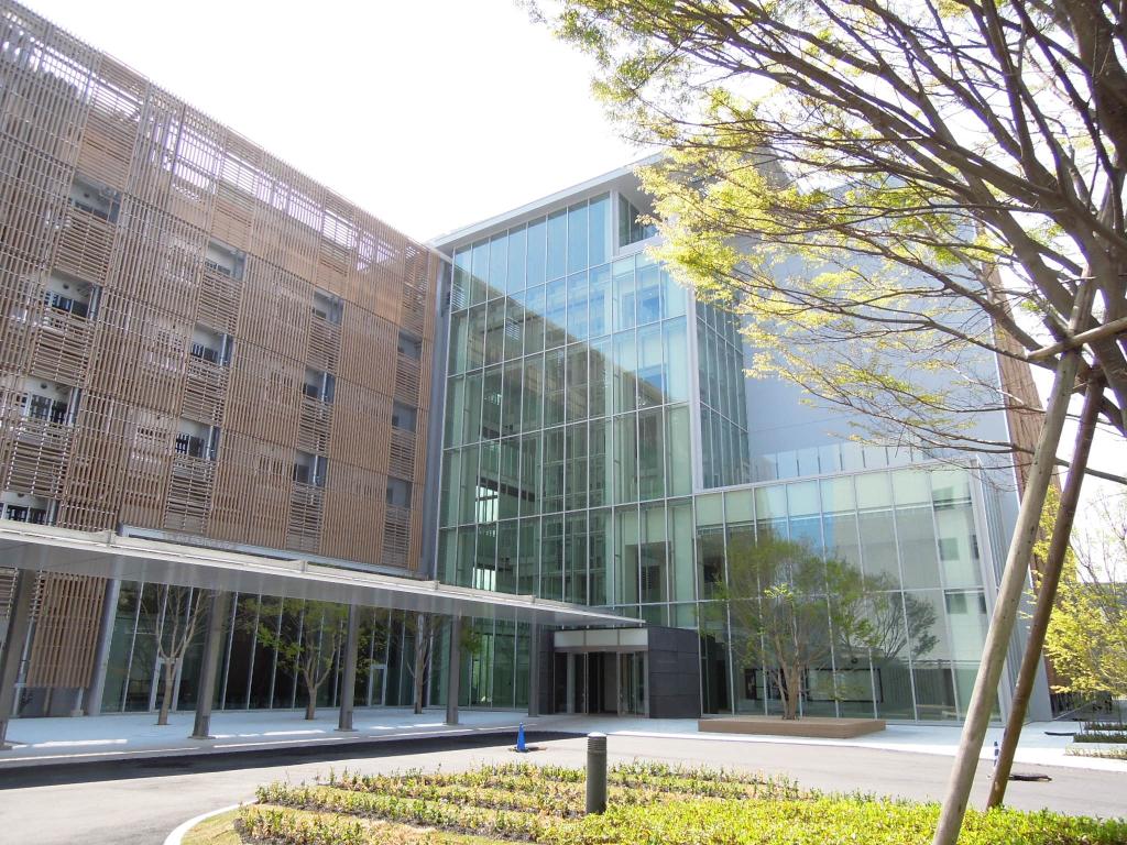 Brick building to the left connected with a glass building on the right. There is a tree in front with a sidewalk and grass