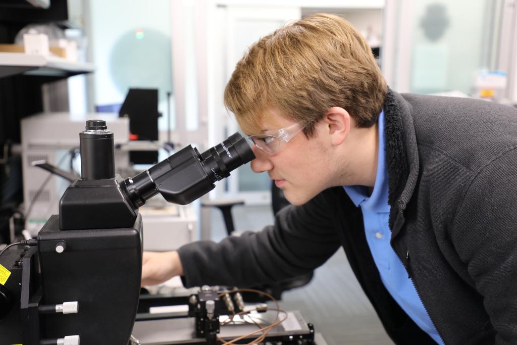 Gage Slacum looks at a circuit board through a microscope. Credit: Josie Fellers/ORNL, U.S. Dept. of Energy