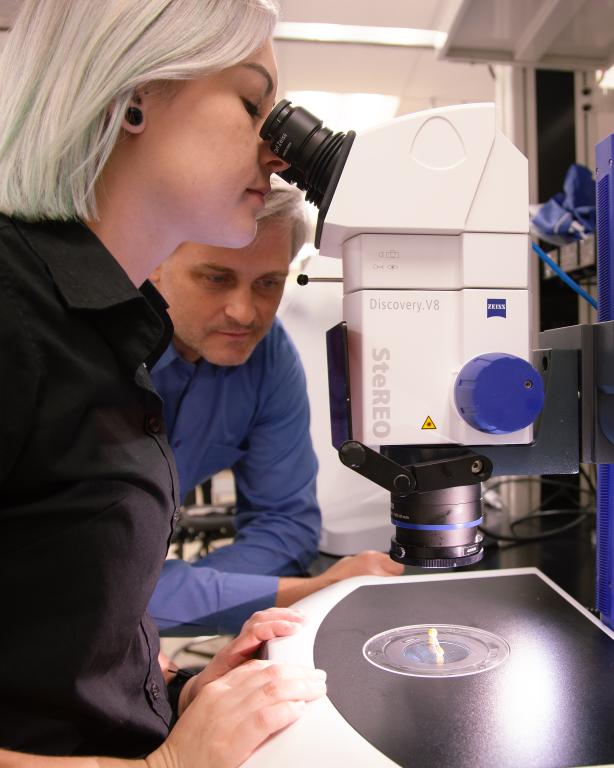 Victoria looking into a microscope and Andrii beside her looking at the crystal sample. 