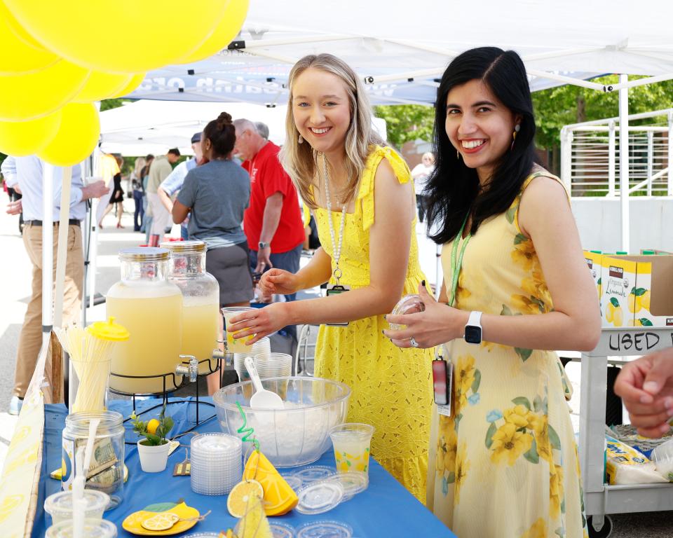 Two women standing behind a lemonade stand preparing cups for employees