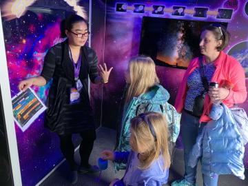 ORNL researcher Chengyun Hua explains chemical elements to Leah Pitts, 9, and her sister Madeline, 6, as their mother, Shayne looks on. The Pittses are part of Pack 50 in the Karns area of Knoxville.