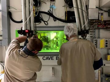 Technicians John Dyer and T. Dyer use a manipulator arm in a shielded cave in ORNL’s Radiochemical Engineering Development Center to separate concentrated Pm-147 from byproducts generated through the production of Pu-238. 
