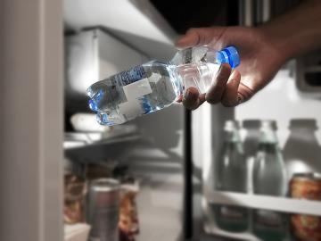 Hand holding water bottle in front of open refrigerator door
