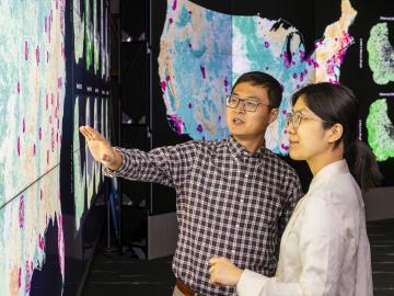 Jiafu Mao, left, and Yaoping Wang discuss their analysis of urban and rural vegetation resilience across the United States in the EVEREST visualization lab at ORNL. Credit: Carlos Jones, ORNL/U.S. Dept. of Energy