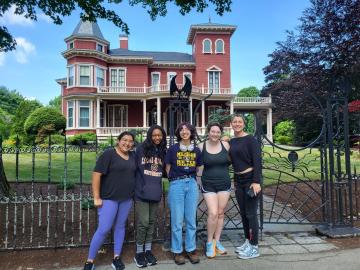 Five girls stand outside of a red brick building with iron gate out front, Stephen King's house. 