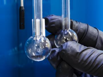 rounded glass beakers held in black rubber gloves in battery lab