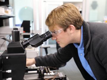 Gage Slacum looks at a circuit board through a microscope. Credit: Josie Fellers/ORNL, U.S. Dept. of Energy