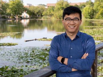 Daryl Yang standing on a bridge overlooking a pond covered in water lillies 