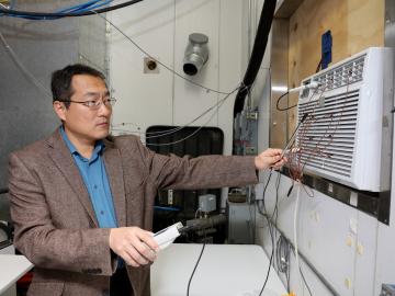 Oak Ridge National Laboratory’s Bo Shen works with a prototype window air conditioning unit that cools using propane, which lowers costs, increases efficiency and benefits the environment.