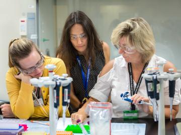 Flora Meilleur (middle) works with teachers participating in her project, helping them mix the protein solution lysozyme with a salt solution to form a crystal. The teachers mix the solutions in various concentrations and ratios and observe the results.