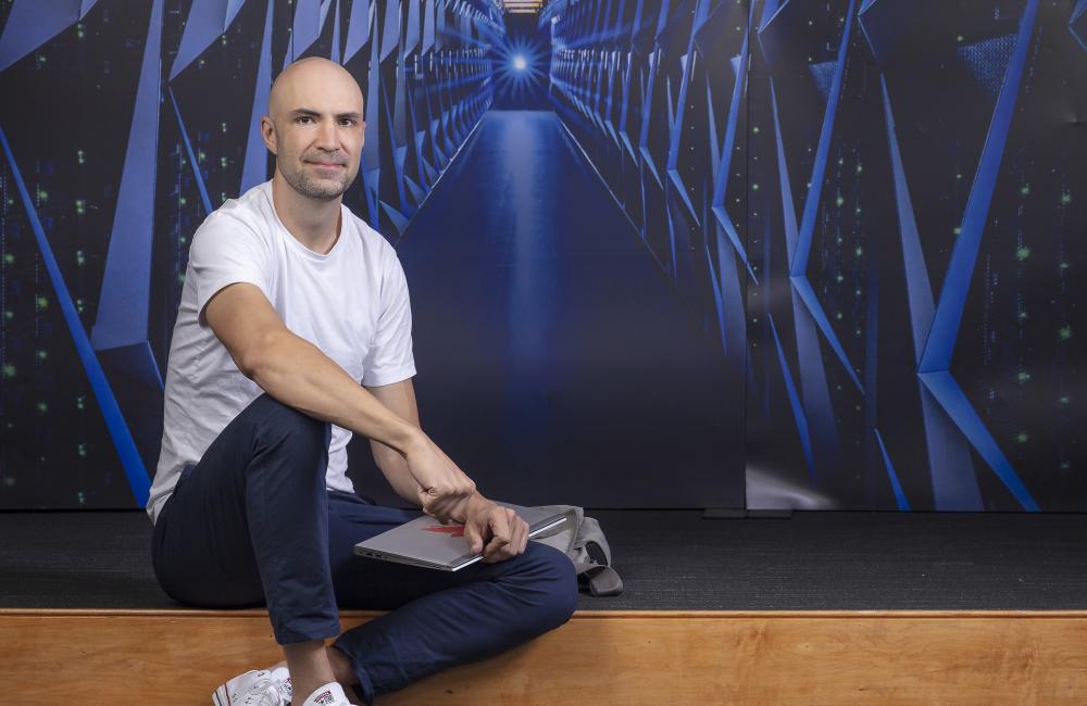 Aaron Ferber poses by a background of Summit, a supercomputer at Oak Ridge National Laboratory
