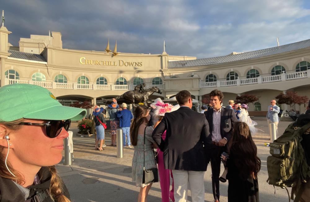 Angie Lousteau, wearing a green hat and sunglasses, takes a selfie outside of the Churchill Downs at the Kentucky Derby. 