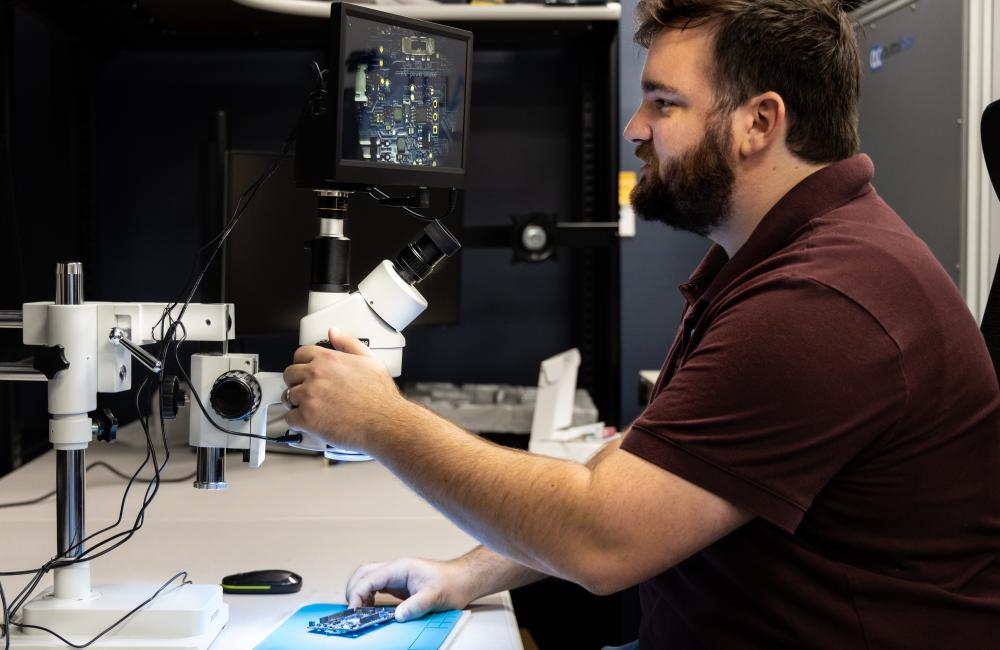 Alex Mullins, a cyber security technical professional at ORNL, deciphers microscopic markings on each chip on a board. Credit: Genevieve Martin/ORNL, U.S. Dept. of Energy