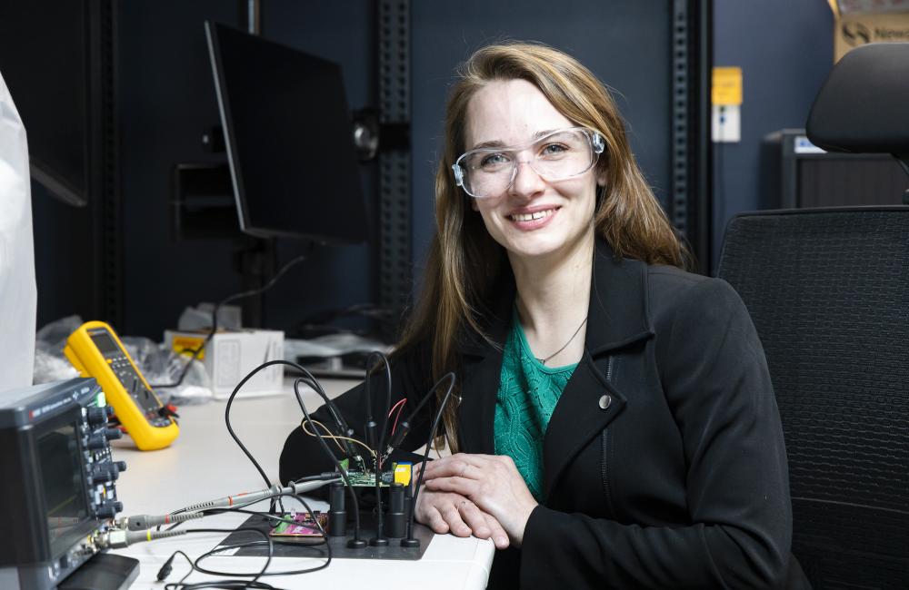 A woman in safety glasses smiles while working on microelectronics