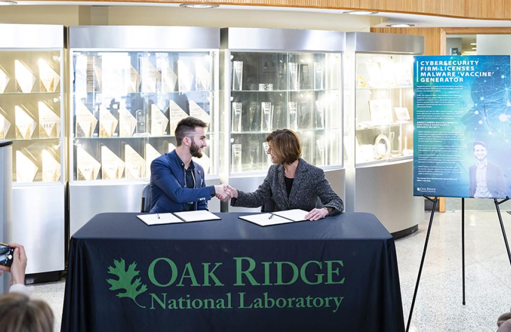 Jared Smith, former ORNL scientist and the inventor of the adversarial malware input generator, or AMIGO, shakes hands with Susan Hubbard, ORNL deputy for science and technology, during an event to celebrate the licensing of AMIGO to Smith's company, Penguin Mustache, on March 21. Credit: Carlos Jones/ORNL, U.S. Dept. of Energy