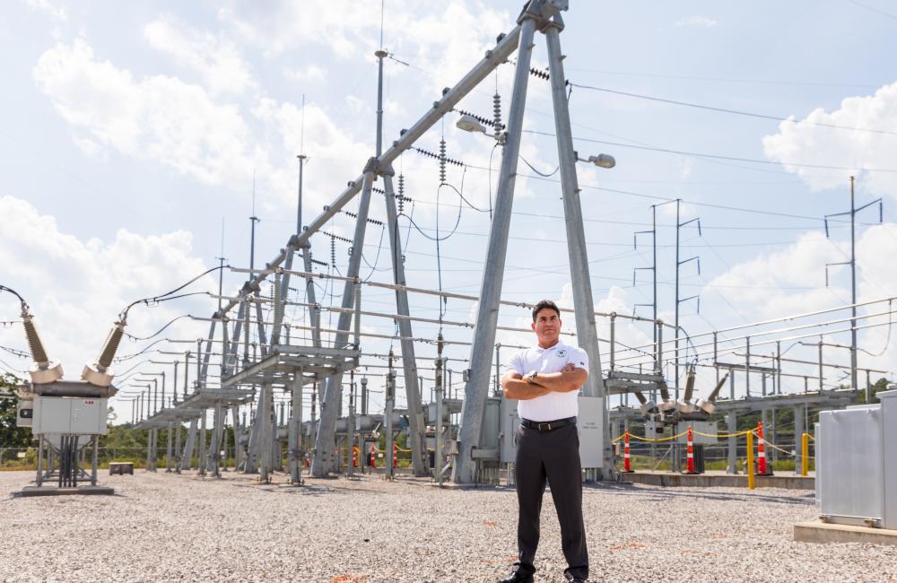 A man stands in front of energy grid substation