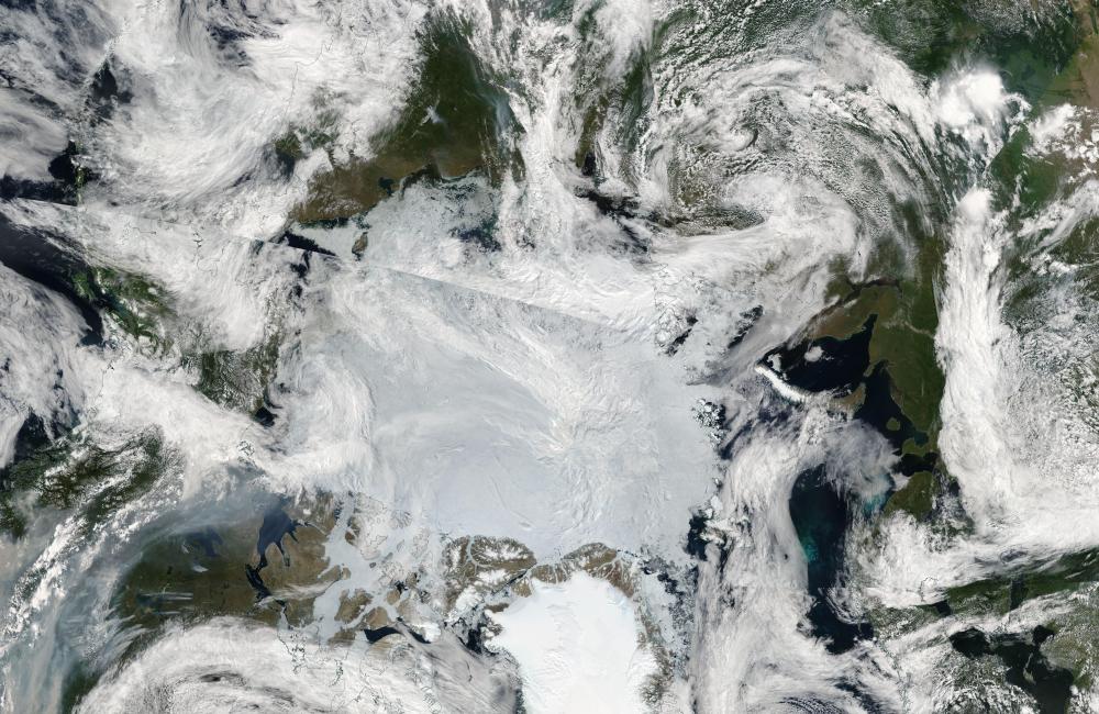 Clouds of gray smoke in the lower left are funneled northward from wildfires in Western Canada, reaching the edge of the sea ice covering the Arctic Ocean.