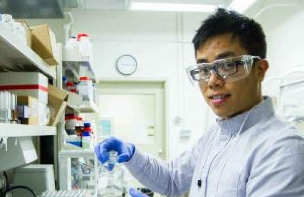 A young man working in a lab space, holding a vial.