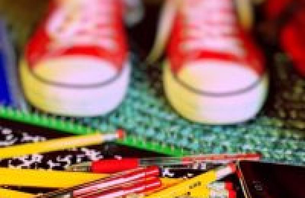 In the background are a child's feet wearing red converse sneakers and the foreground is a pile of pencils, pens, notebooks and a calculator. 