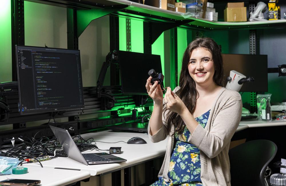 A woman working in a cyber laboratory smiles at the camera while holding research equipment