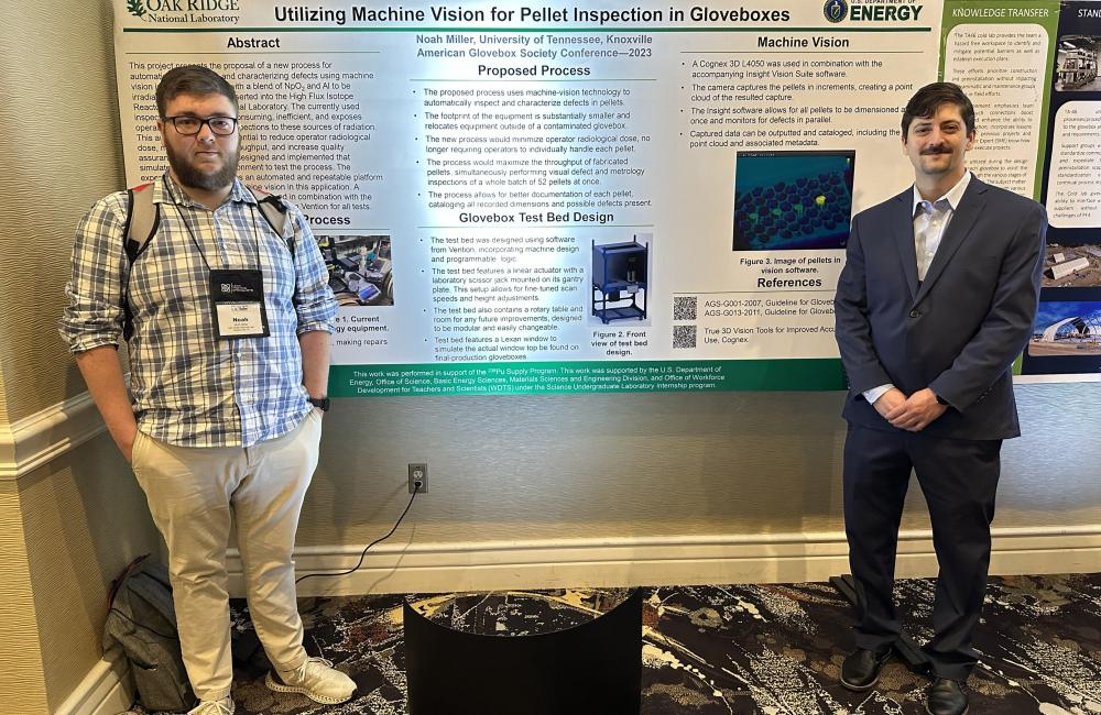 Intern Noah Miller, left, and his mentor, Joe McVeigh, stand with their poster at the American Glovebox Society conference in 2023.